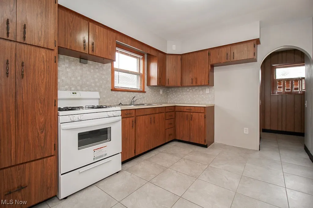 Kitchen featuring white gas range oven, tasteful backsplash, brown cabinetry, and light countertops