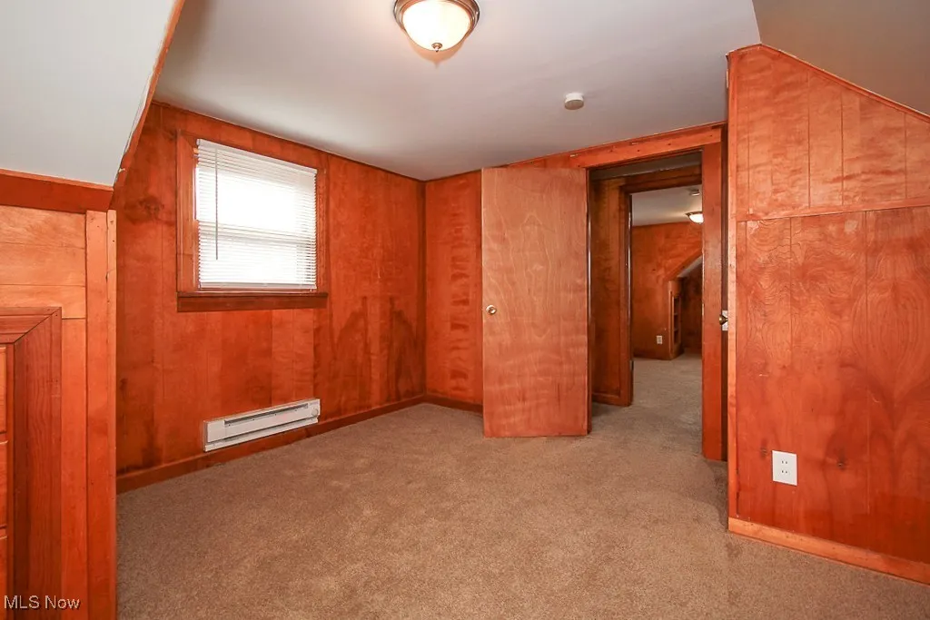 Empty room featuring baseboard heating, carpet, wooden walls, and a smoke detector
