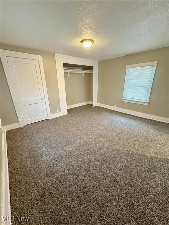 Unfurnished bedroom with a textured ceiling, a closet, and dark carpet
