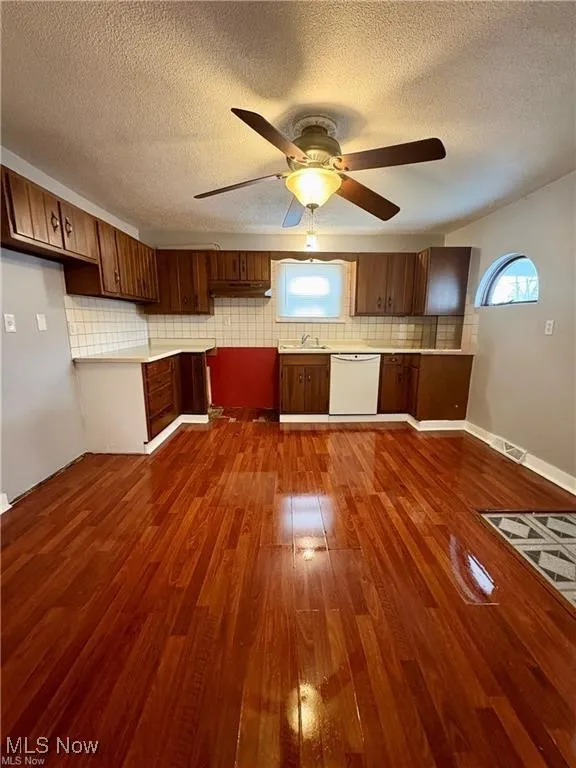 Kitchen with white dishwasher, dark wood-type flooring, light countertops, backsplash, and a textured ceiling