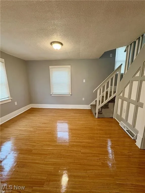 Unfurnished living room featuring stairway, a textured ceiling, and wood finished floors