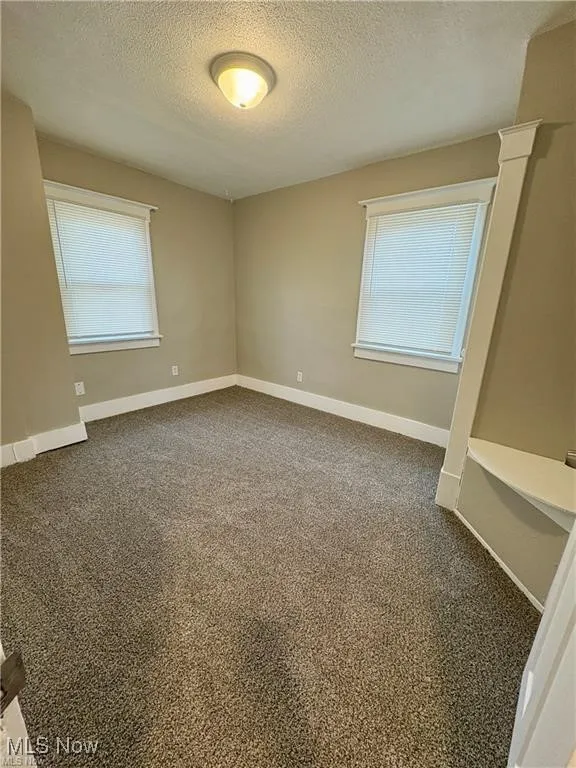 Unfurnished room featuring a textured ceiling, healthy amount of natural light, and dark carpet