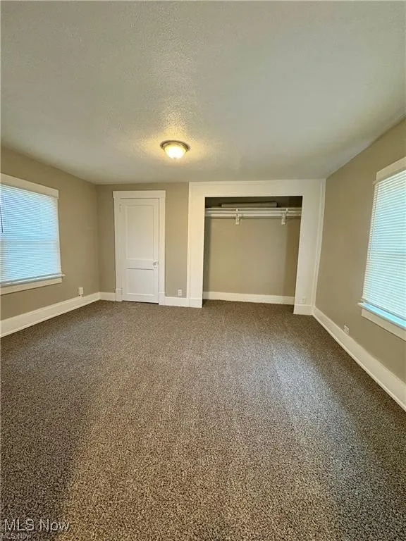 Unfurnished bedroom with multiple windows, a closet, a textured ceiling, and dark colored carpet