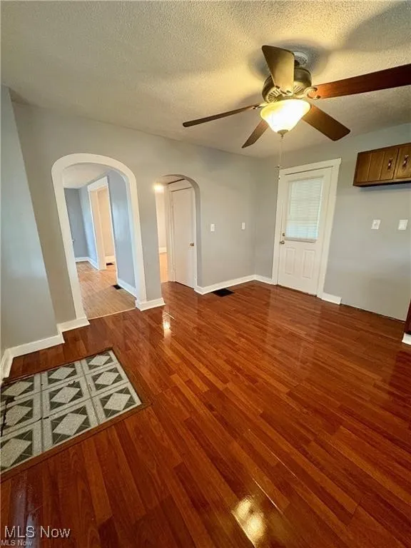 Unfurnished living room featuring arched walkways, ceiling fan, wood finished floors, and a textured ceiling