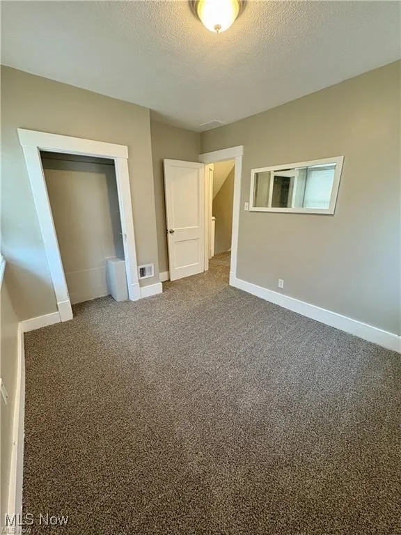 Unfurnished bedroom with a textured ceiling, a closet, and carpet