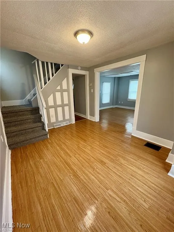 Spare room with light wood-style flooring, stairway, and a textured ceiling
