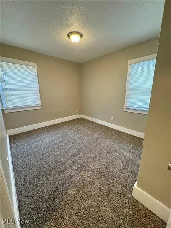Unfurnished room featuring a textured ceiling, dark colored carpet, and healthy amount of natural light