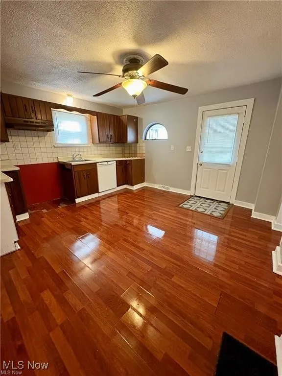 Kitchen featuring dishwasher, decorative backsplash, dark wood-style floors, healthy amount of natural light, and a textured ceiling