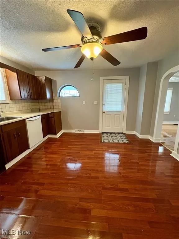 Kitchen with dishwasher, arched walkways, a ceiling fan, a textured ceiling, and decorative backsplash