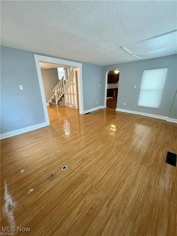 Spare room with arched walkways, a textured ceiling, wood finished floors, and stairway