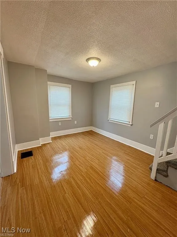Empty room with light wood finished floors, a textured ceiling, and stairs