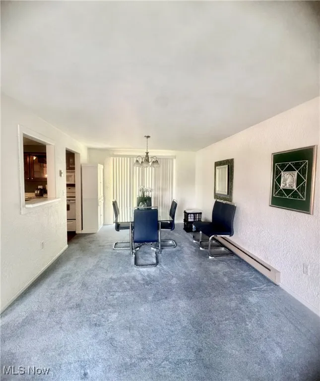 Dining room with a chandelier, a textured wall, carpet flooring, and a baseboard radiator