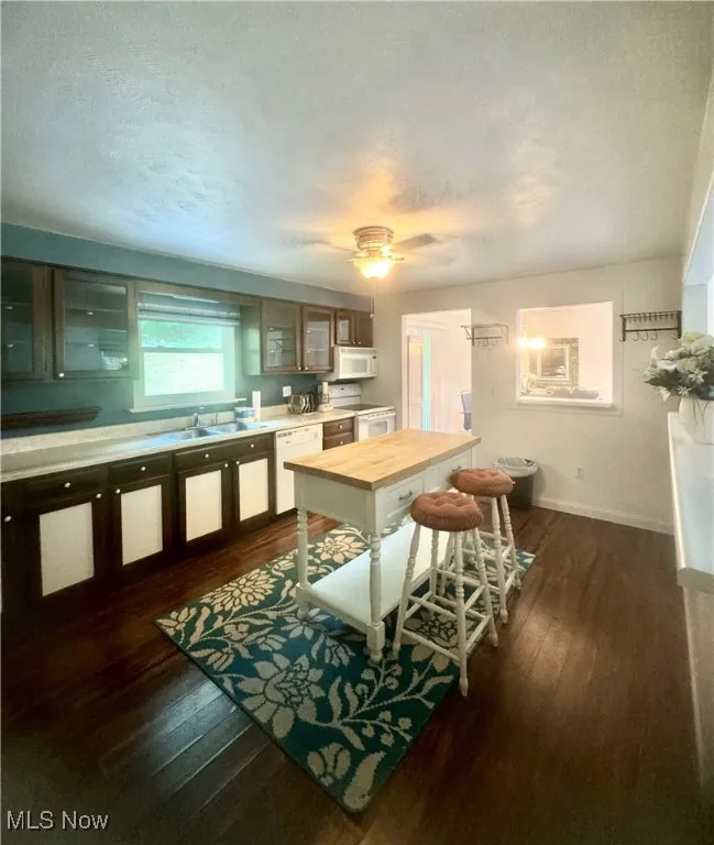 Kitchen featuring white appliances, dark wood finished floors, a textured ceiling, glass insert cabinets, and butcher block countertops