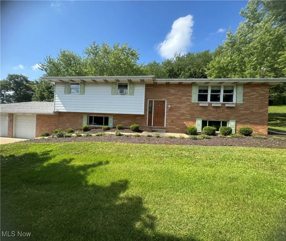 Raised ranch with brick siding, a front lawn, and a garage
