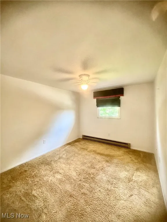 Spare room featuring a baseboard heating unit, carpet floors, and a ceiling fan