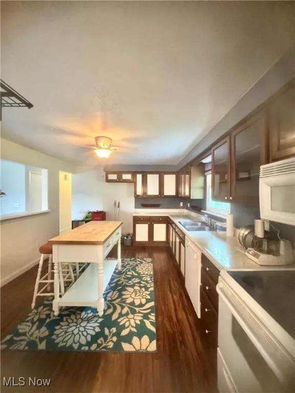 Kitchen with white appliances, dark wood-style flooring, butcher block counters, and glass insert cabinets