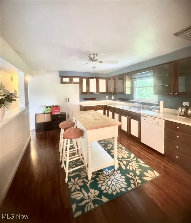 Kitchen with white dishwasher, dark wood-style flooring, light countertops, glass insert cabinets, and a ceiling fan