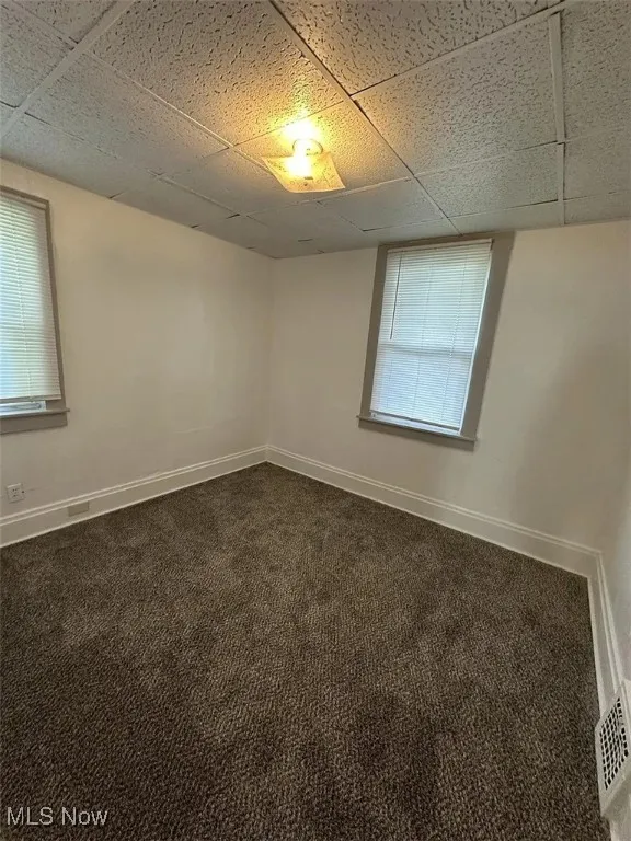Spare room with dark carpet and a paneled ceiling