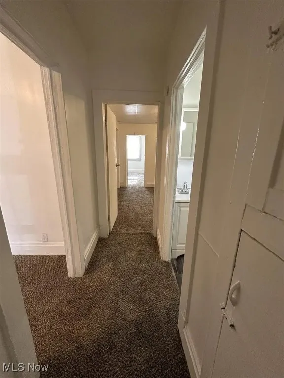 Corridor featuring dark carpet and baseboards