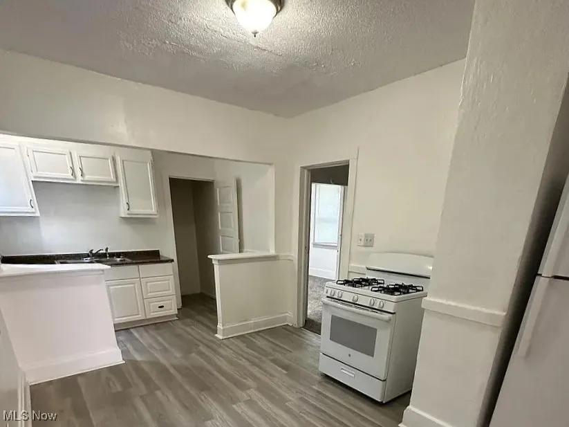 Kitchen featuring white range with gas stovetop, dark wood-style floors, white cabinets, and a textured ceiling