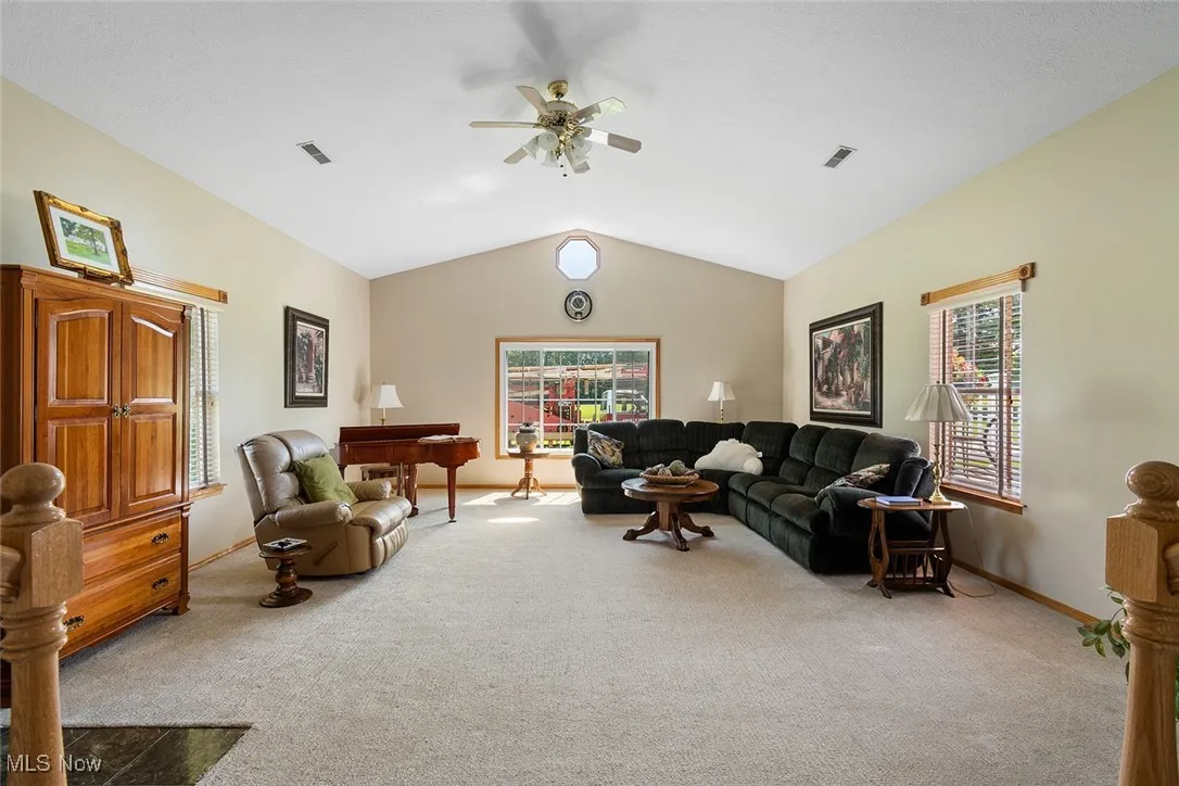 Carpeted living room with a ceiling fan and lofted ceiling