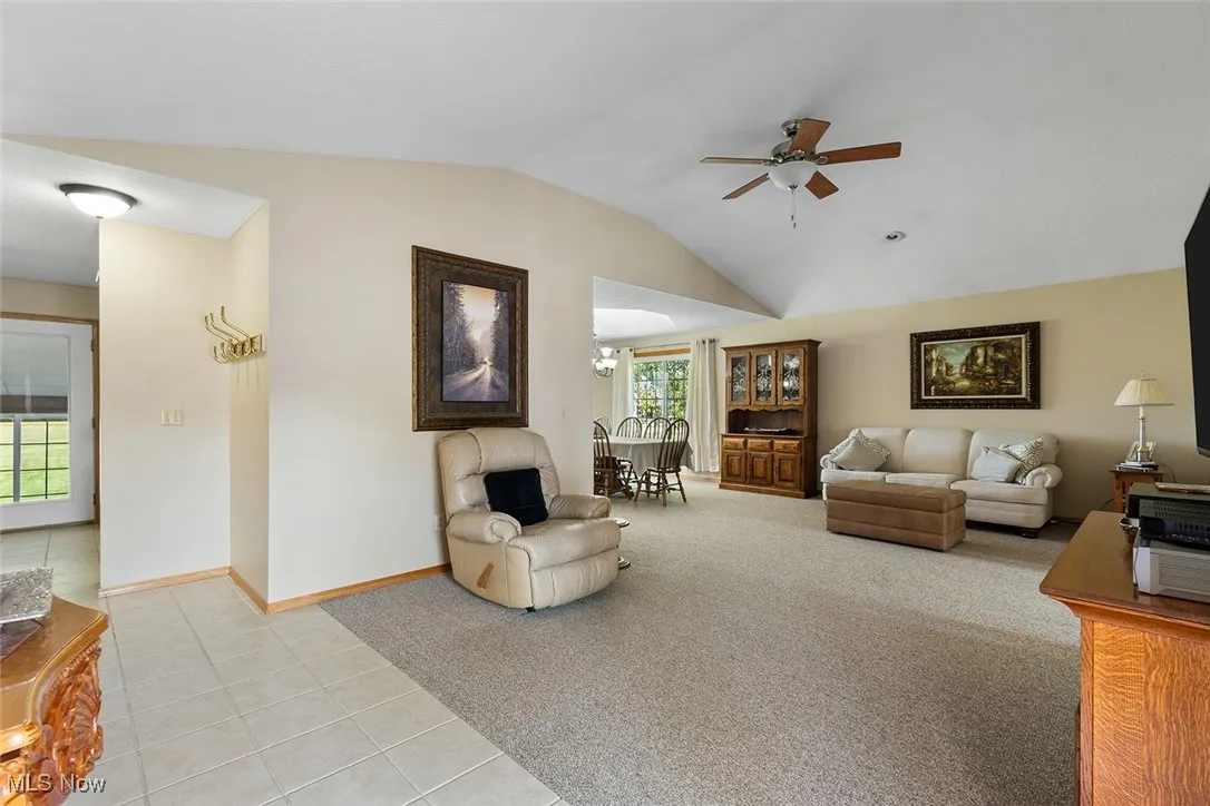 Living area featuring a ceiling fan, lofted ceiling, light tile patterned floors, and light carpet
