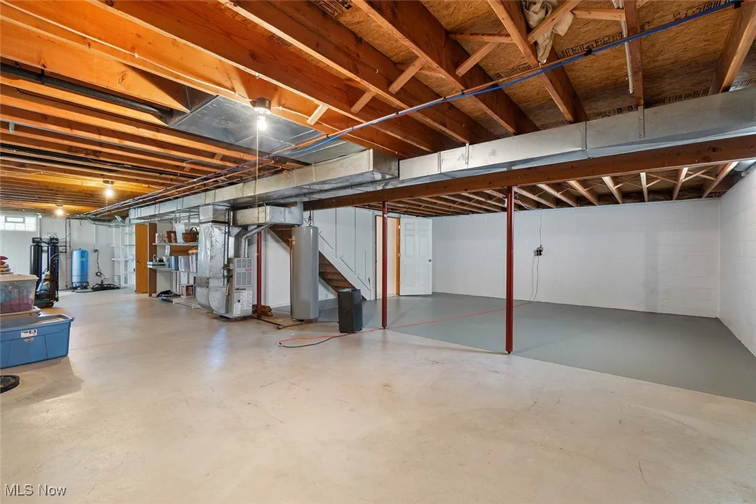 Below grade area featuring water heater, stairway, heating unit, and concrete block wall