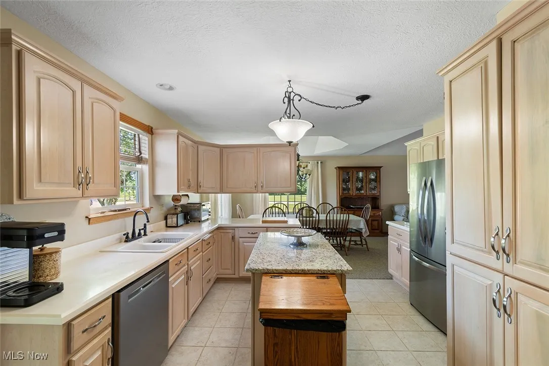 Kitchen featuring appliances with stainless steel finishes, light brown cabinetry, a kitchen island, light countertops, and a peninsula