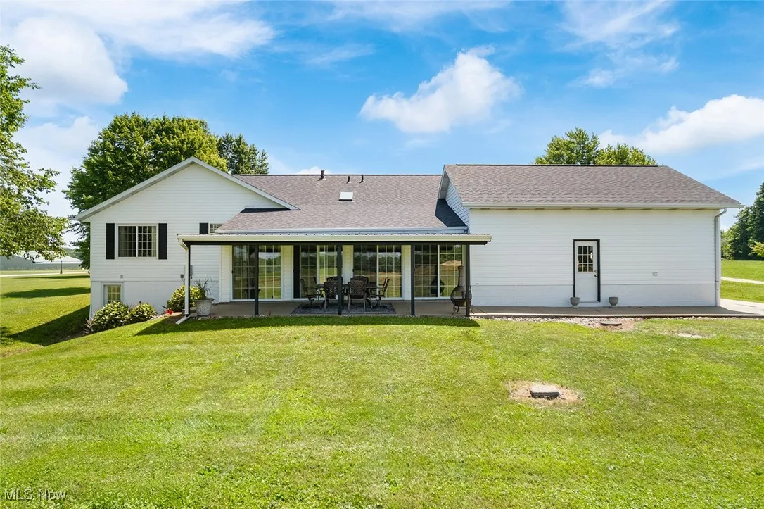 Rear view of property with a yard, a patio area, roof with shingles, and a sunroom