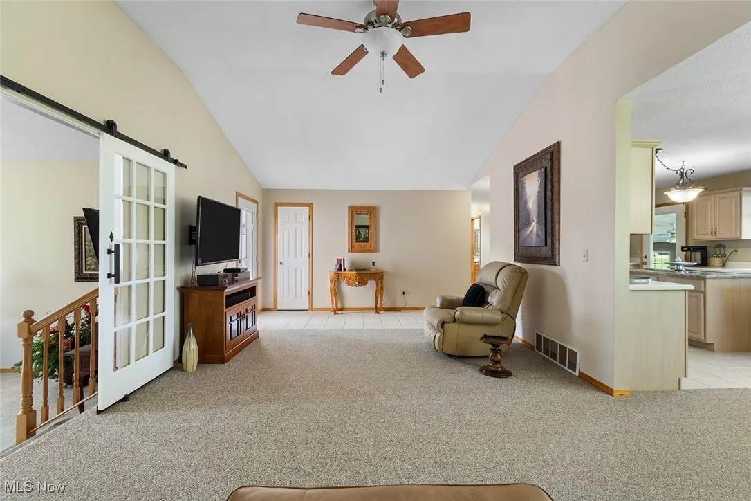 Living area with lofted ceiling, light colored carpet, and a ceiling fan