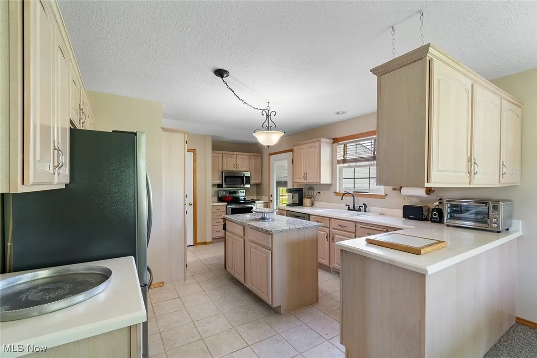 Kitchen featuring appliances with stainless steel finishes, light brown cabinetry, light countertops, a peninsula, and light tile patterned flooring