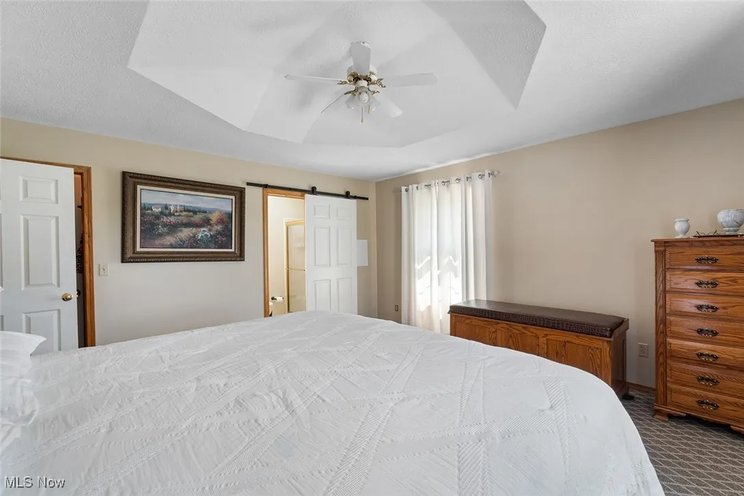 Bedroom featuring dark carpet, a barn door, a tray ceiling, and ceiling fan