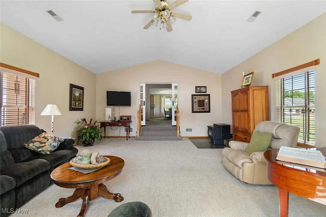 Carpeted living area with lofted ceiling, a ceiling fan, and a wood stove