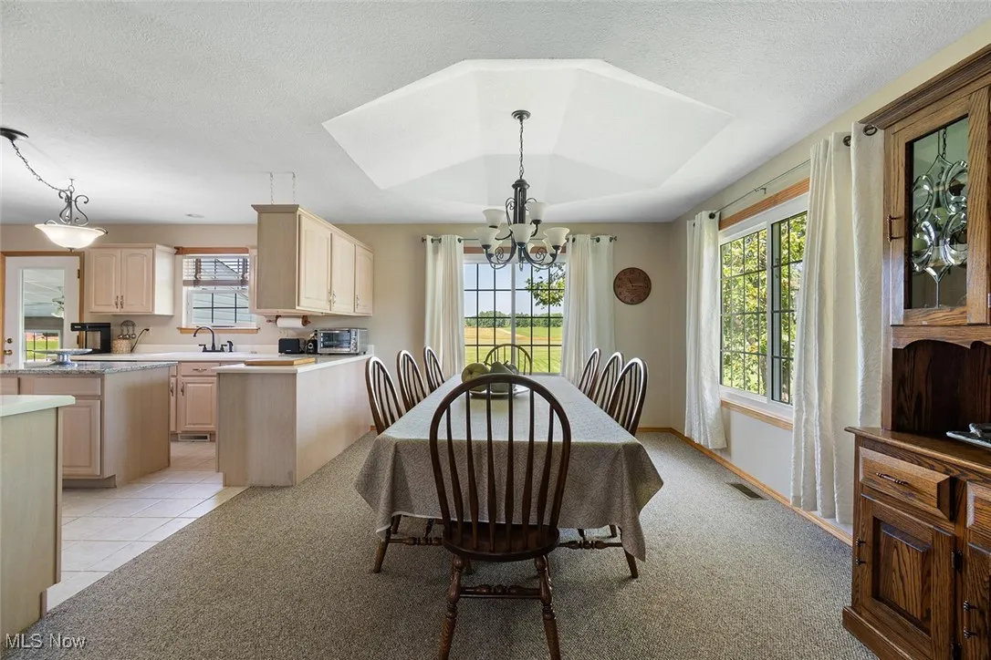 Dining space with a chandelier, light colored carpet, light tile patterned floors, and a textured ceiling