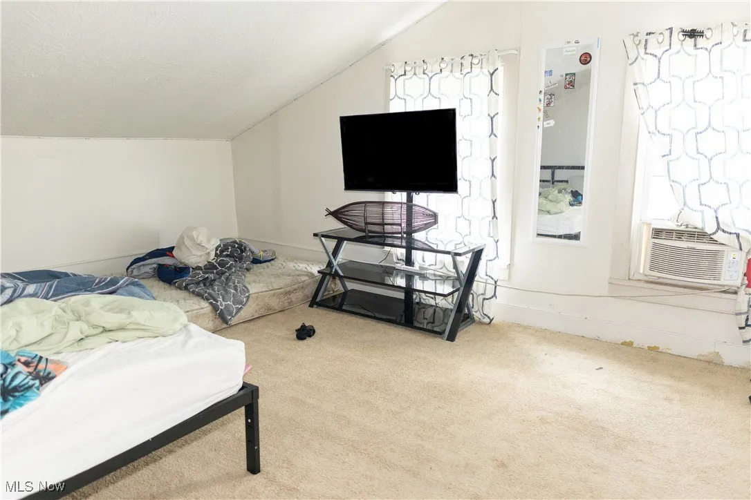 Carpeted bedroom with lofted ceiling and cooling unit