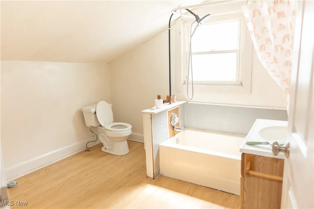 Full bath featuring a tub to relax in, wood finished floors, vanity, and vaulted ceiling