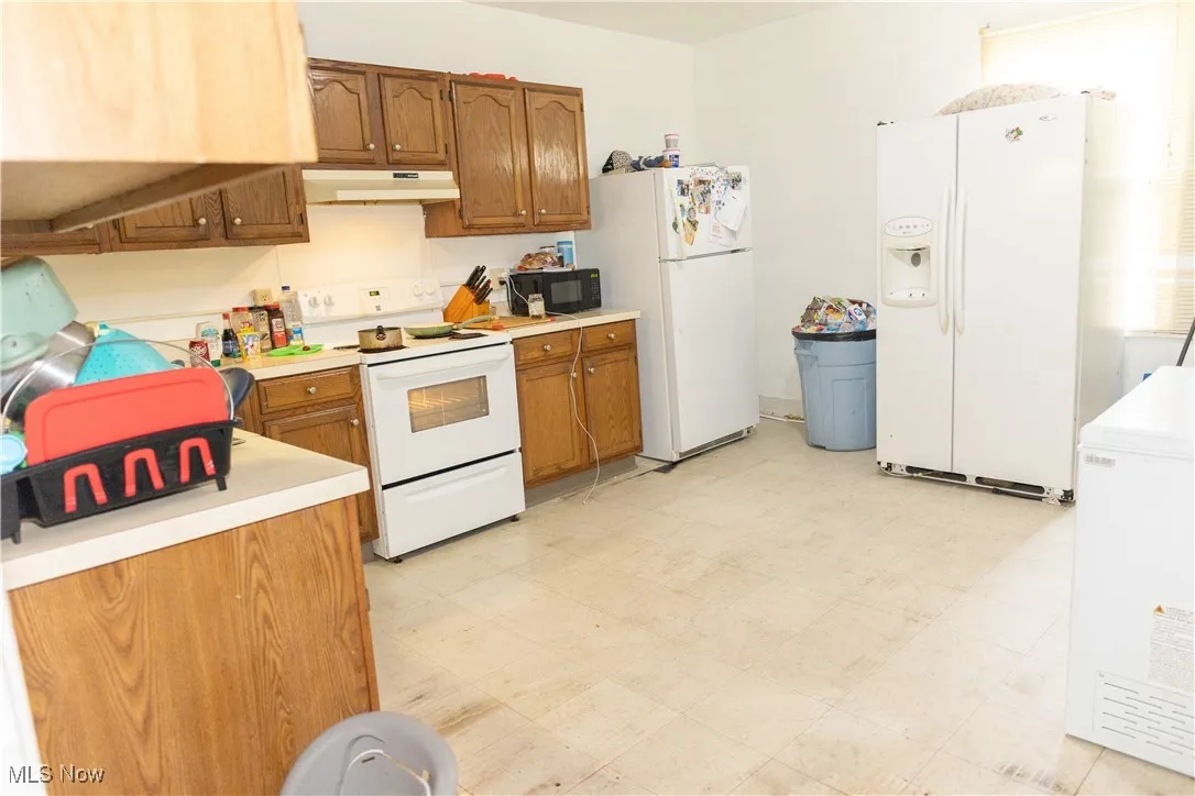 Kitchen featuring white appliances, under cabinet range hood, light countertops, and brown cabinetry