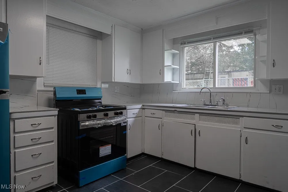 Kitchen featuring gas range, ornamental molding, white cabinetry, backsplash, and dark tile patterned flooring