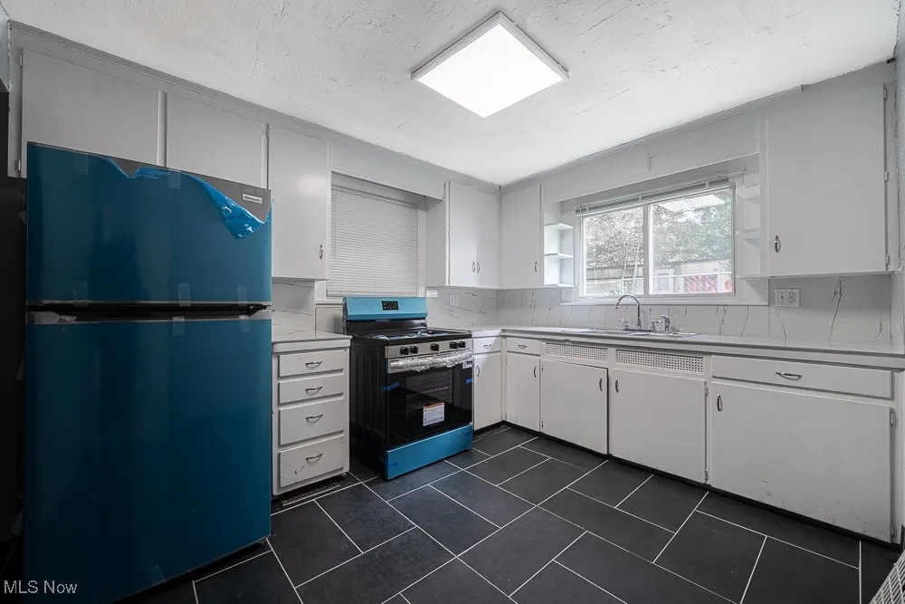 Kitchen featuring refrigerator, stainless steel gas stove, light countertops, decorative backsplash, and white cabinets
