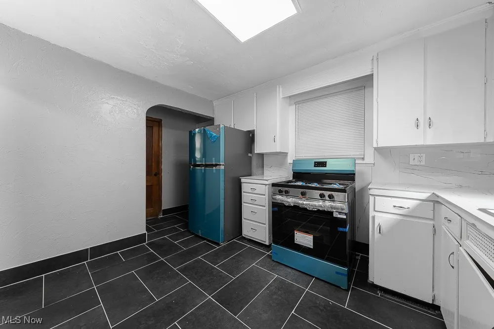 Kitchen with stainless steel gas stove, freestanding refrigerator, white cabinets, a textured wall, and light countertops