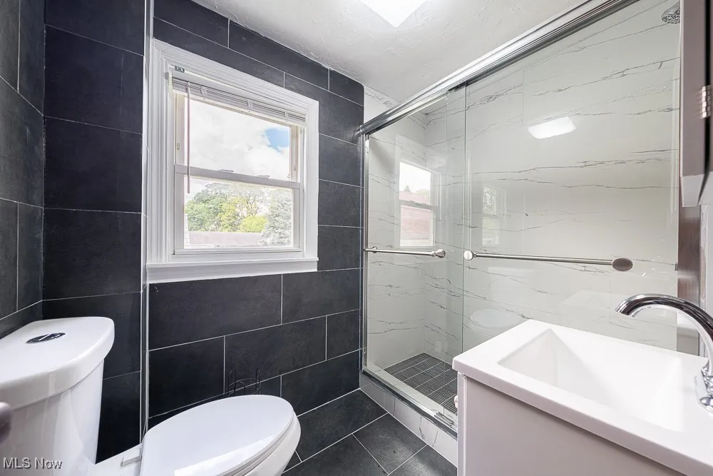 Full bathroom featuring tile walls, a marble finish shower, tile patterned flooring, and vanity