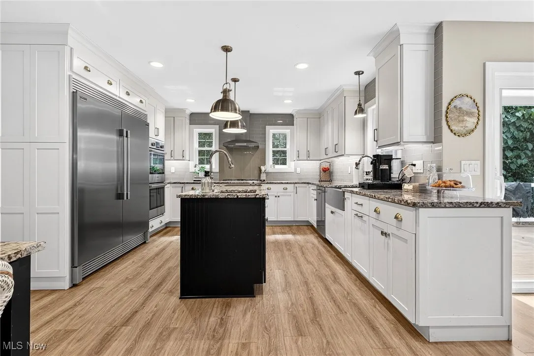 Kitchen with stainless steel appliances, dark stone countertops, an island with sink, decorative backsplash, and recessed lighting