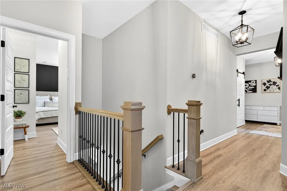 Corridor featuring an upstairs landing, light wood finished floors, a chandelier, and a barn door