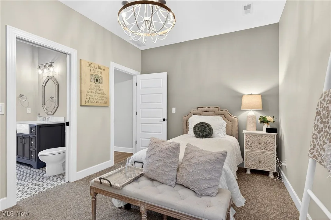 Carpeted bedroom featuring a chandelier and ensuite bath