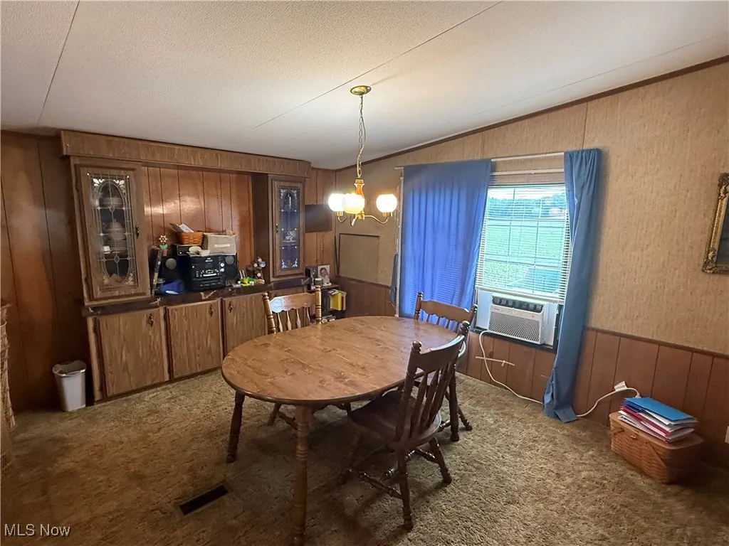 Dining area with carpet floors, wooden walls, cooling unit, lofted ceiling, and a chandelier