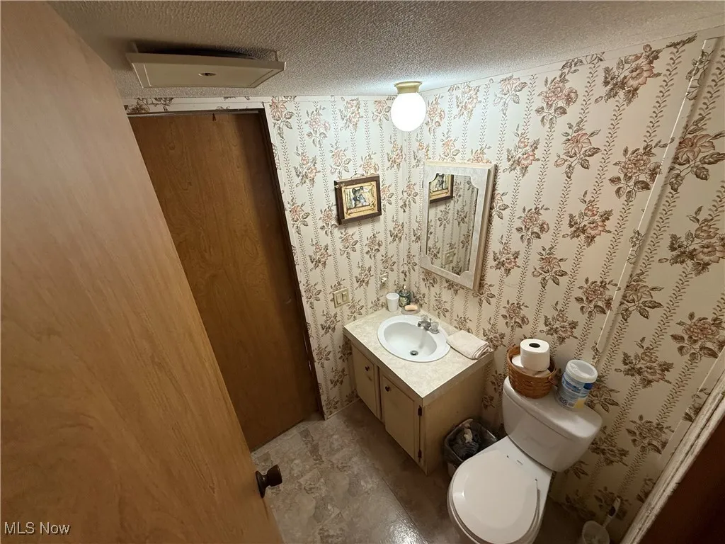 bathroom featuring vanity, a textured ceiling, and wallpapered walls