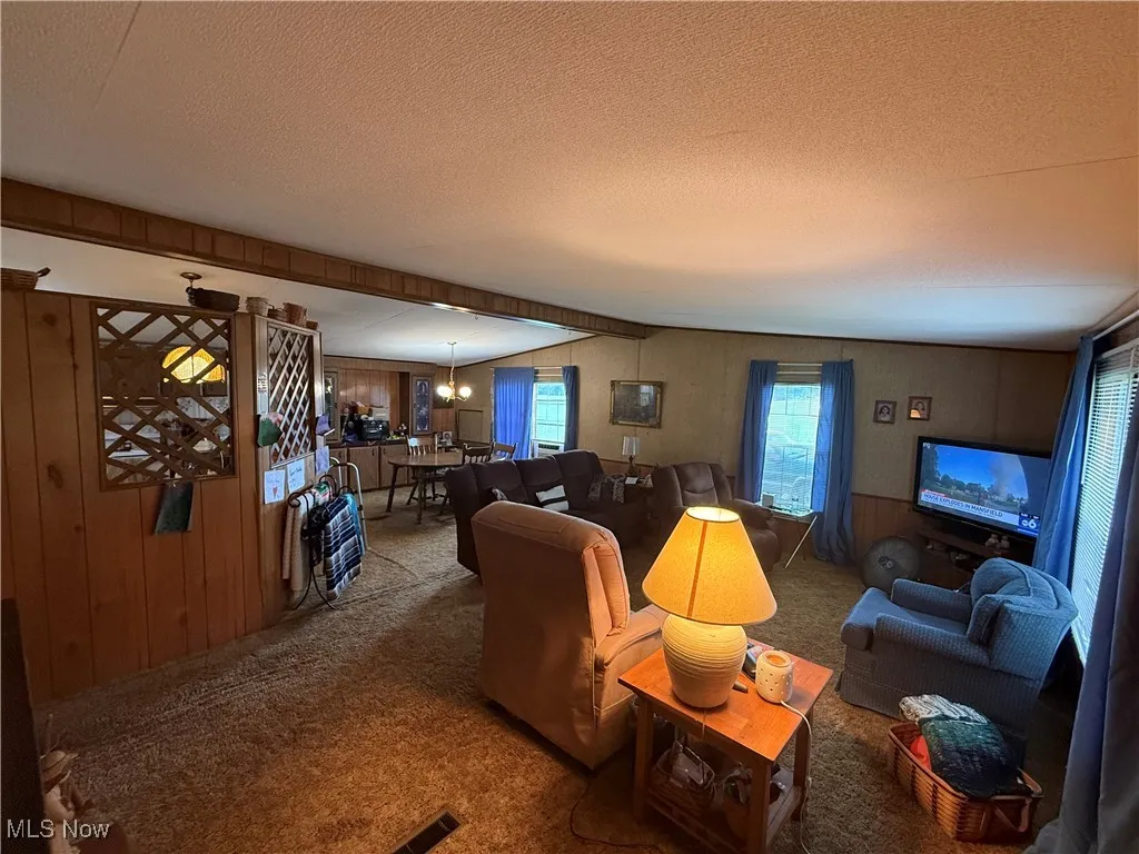 Living area with carpet floors, a textured ceiling, wood walls, and a chandelier