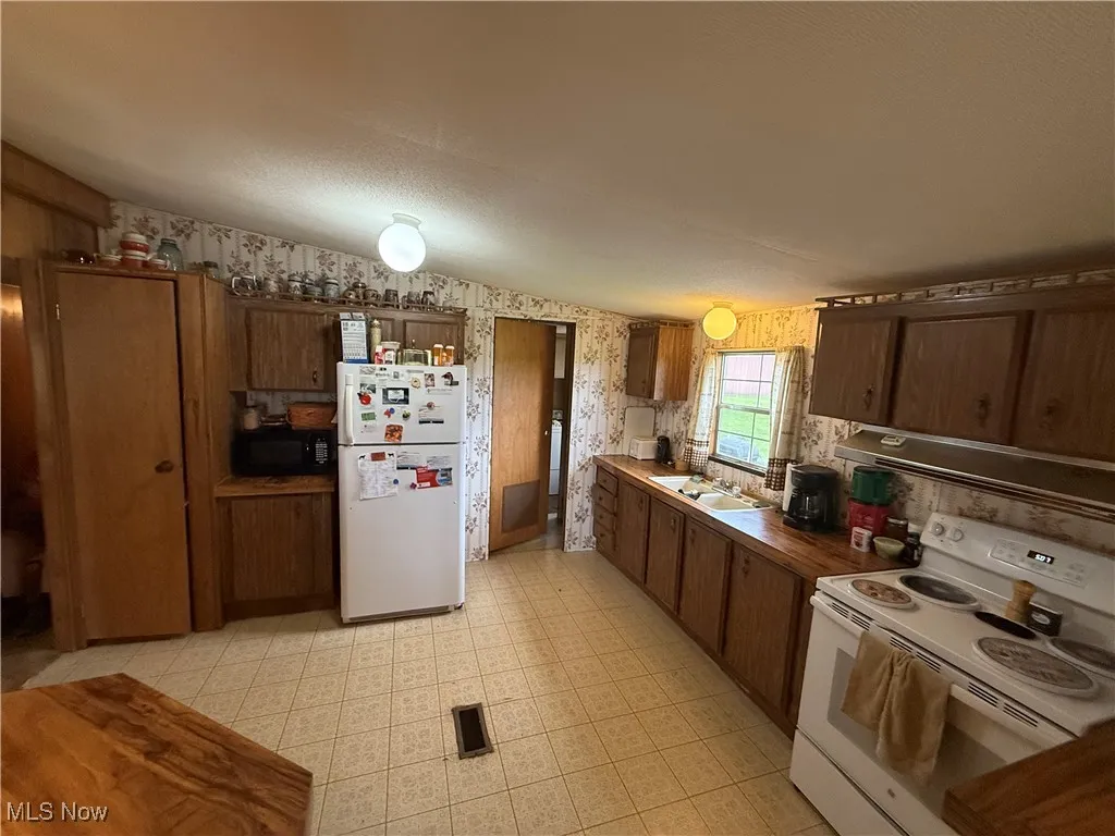 Kitchen with white appliances, wallpapered walls, range hood, and light flooring
