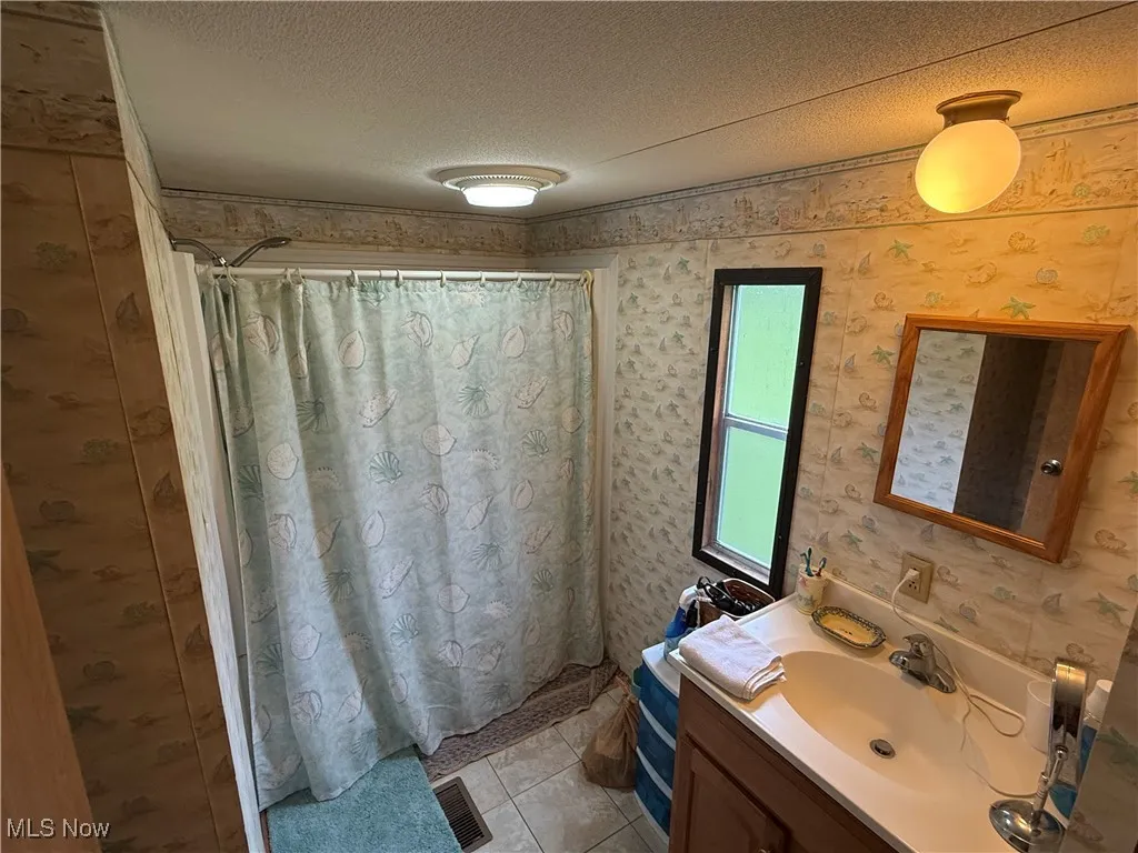 Bathroom featuring vanity, a textured ceiling, wallpapered walls, tile patterned flooring, and a shower with curtain