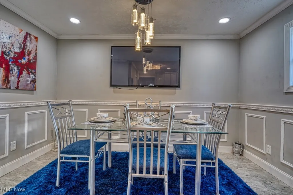 Dining area featuring a decorative wall, crown molding, recessed lighting, and marble finish floors